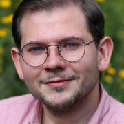 Porträt von Dozent Thomas Odemer, Mann mit Brille und braunen Haaren in rosa Hemd, im Hintergrund Blumenwiese