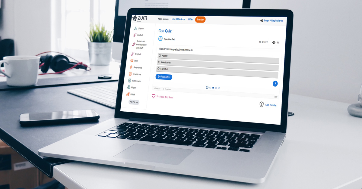 Ein Computer, eine Tasse und Kopfhörer liegen auf einem Schreibtisch.