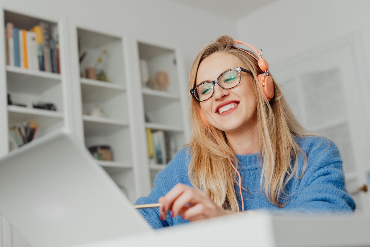 Frau mit blauem Pulli und Kopfhörern vor einem Laptop sitzend